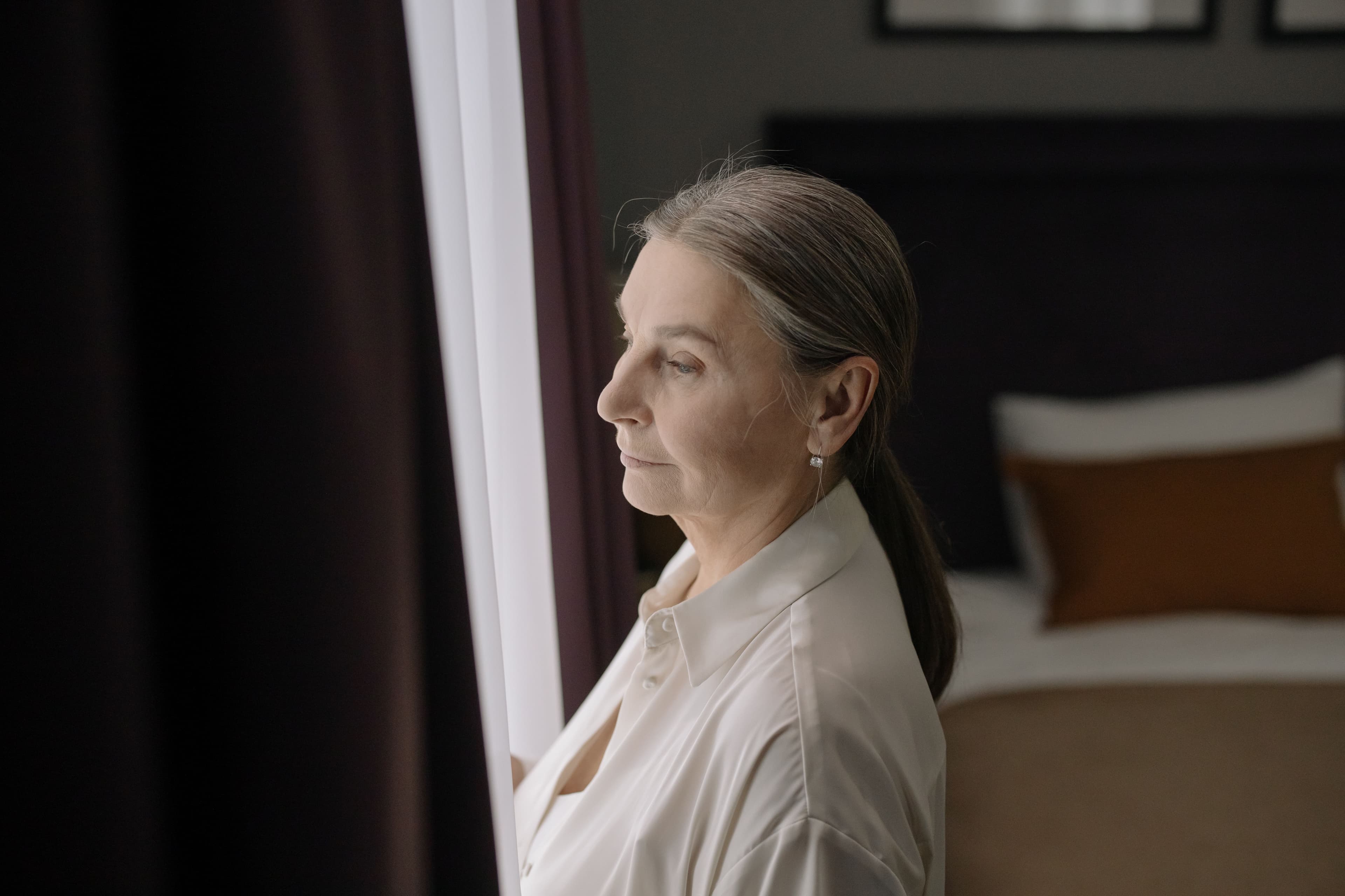 A woman standing beside a window and looking outside, reflecting on her choices and sense of self.
